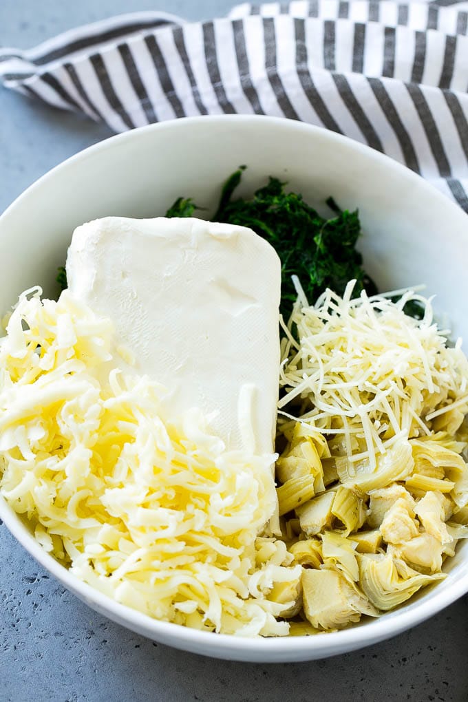 Crema de queso, espinacas, alcachofas y queso rallado en un bol.