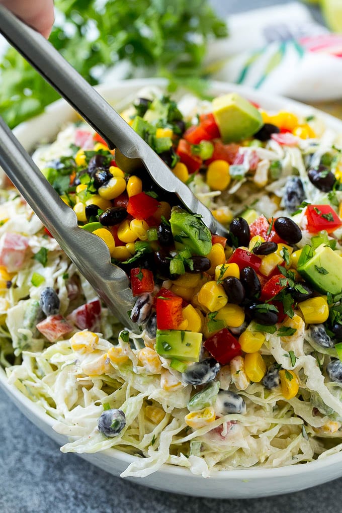Un tazón de ensalada de col mexicana con pinzas para ensalada.
