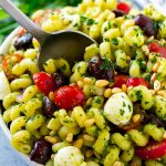 Ensalada de pasta al pesto con tomates cherry, aceitunas, mozzarella, piñones y cebolla morada.