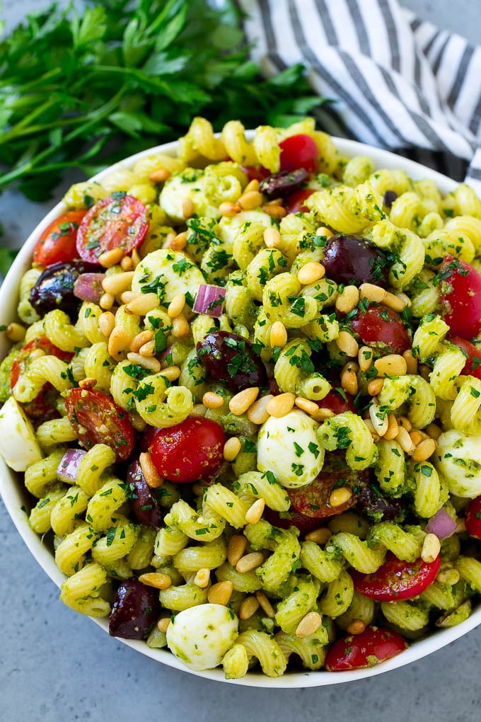 Un plato de ensalada de pasta al pesto aderezado con piñones y perejil picado.