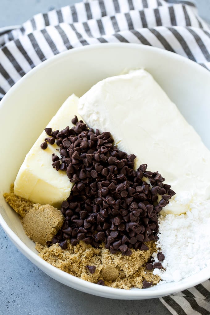 Ingredientes para la salsa de masa para galletas que incluyen mantequilla, queso crema, chispas de chocolate y azúcar morena.