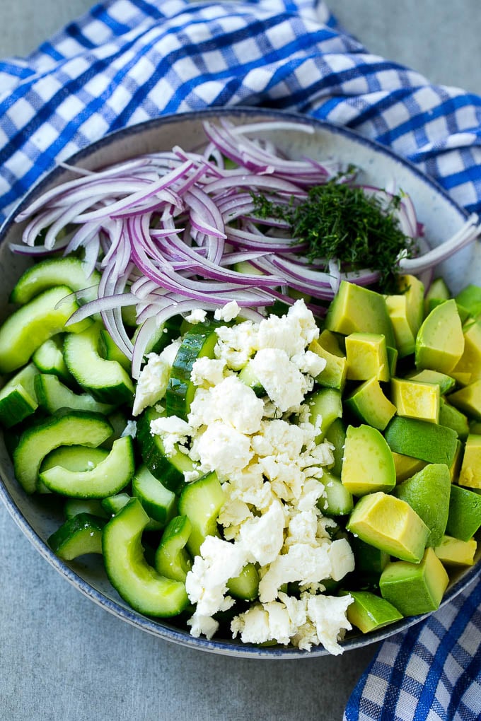 Pepinos, queso feta, aguacate y cebolla morada en un bol.