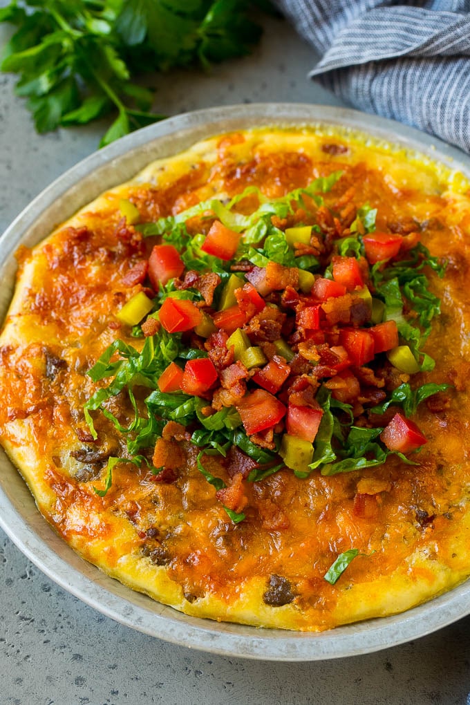 Pastel de hamburguesa con queso cubierto con tocino, lechuga, pepinillos y tomates.