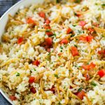 Arroz casero a roni aderezado con tomates cherry y hierbas aromáticas, todo en una sartén.