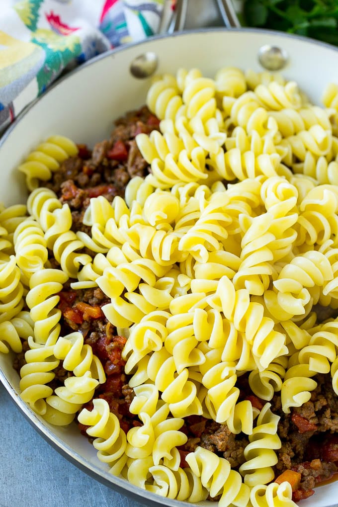 Una sartén de carne molida cocida cubierta con tomates y pasta rotini.