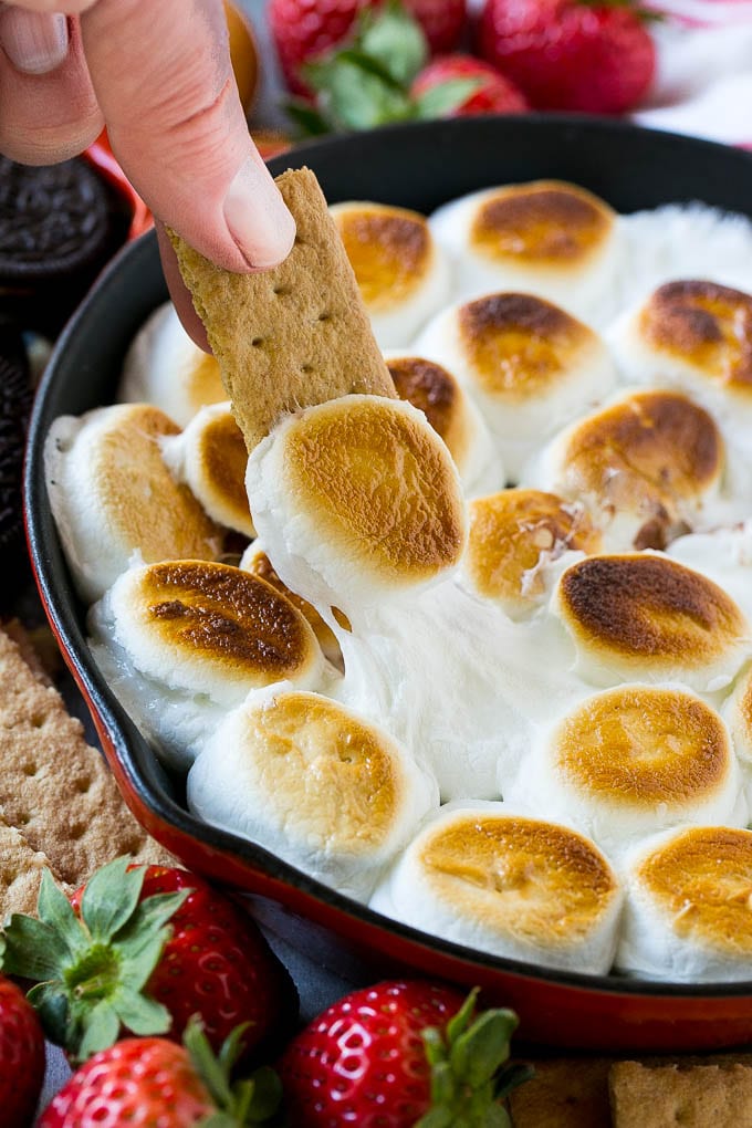 Una galleta Graham cubierta con malvavisco derretido sumergido en una sartén con salsa s'mores.