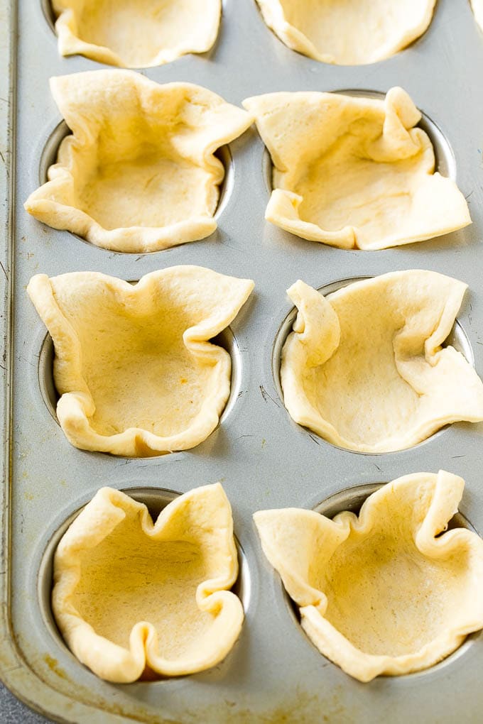 La masa de media luna presionada en un molde para muffins forma la corteza de las magdalenas de pizza.
