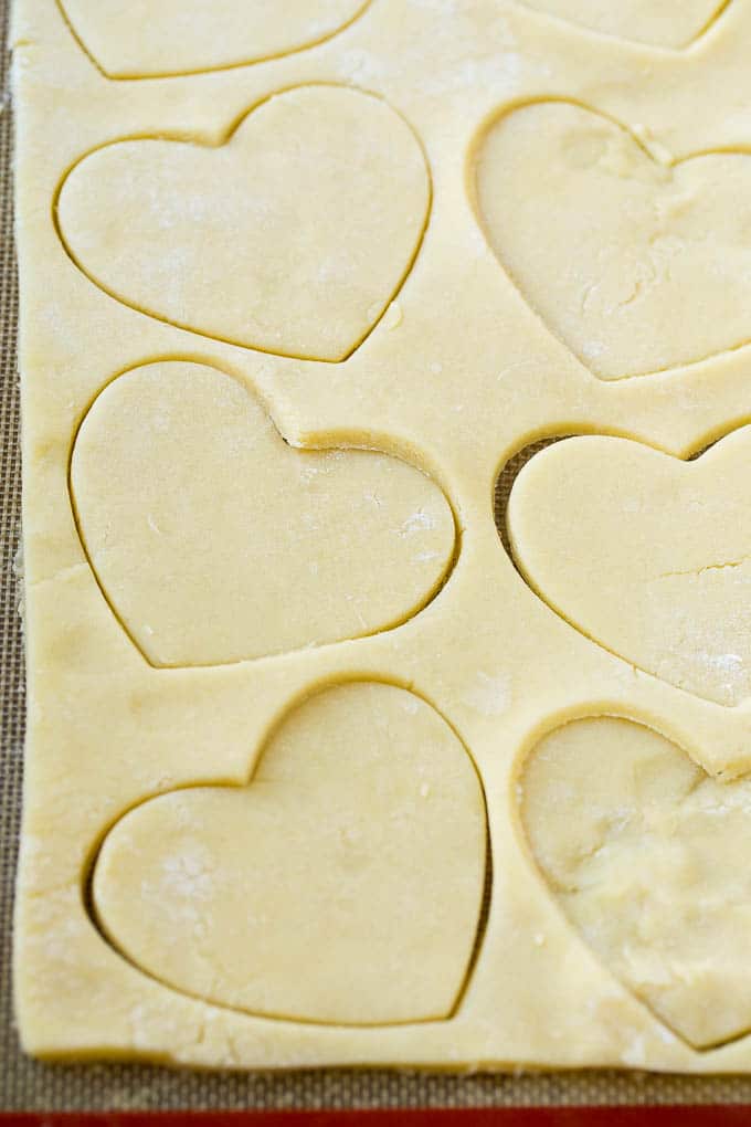 Receta de galletas de corazón | Galletas de azúcar de corazón | Galletas de San Valentín | Galletas de azúcar en forma de corazón | Postre de San Valentín #corazones #cookies #sugarcookies #valentinesday #sprinkles #dessert #dinneratthezoo Una hoja de masa para galletas de azúcar con recortes en forma de corazón.