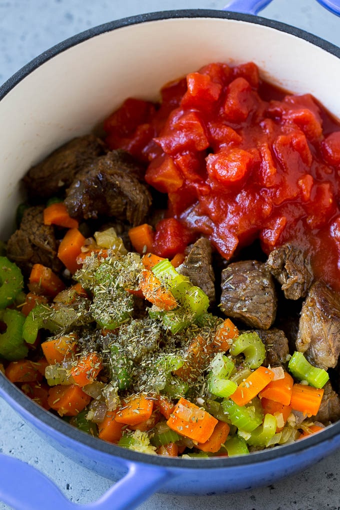 Trozos de carne, verduras, tomates y hierbas en una sartén.