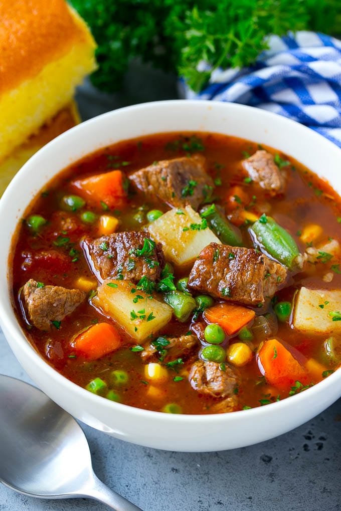 Un plato de sopa de carne con verduras, zanahorias, apio, cebollas, patatas, tomates, maíz y guisantes.