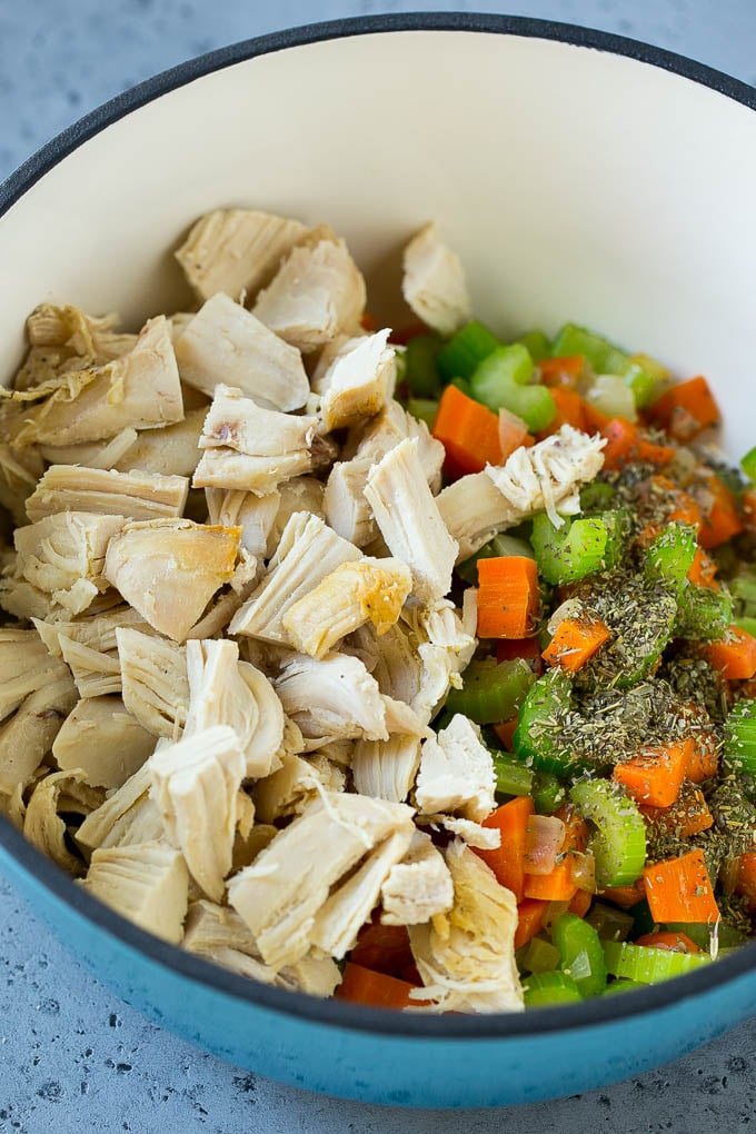 Verduras, pollo rallado y hierbas secas en una tetera.