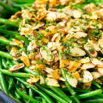 Una cazuela de judías verdes con almendras cubiertas con almendras tostadas en rodajas, mantequilla y perejil picado.