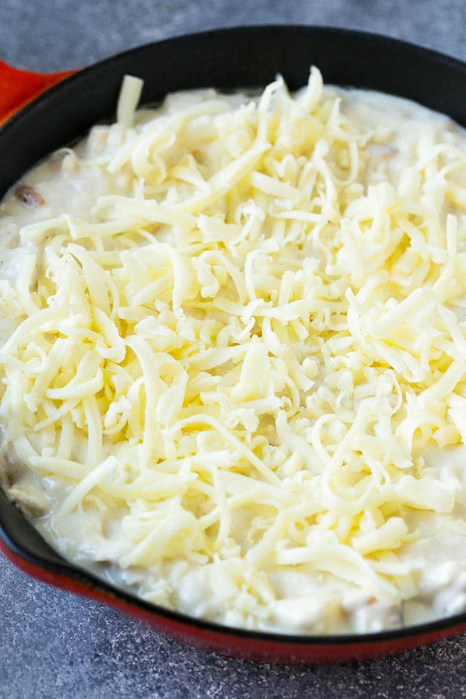 Una sartén de salsa de pollo Alfredo cubierta con mozzarella rallada.