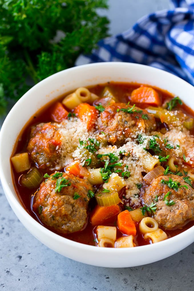 Un plato de sopa de albóndigas cubierto con perejil picado y queso rallado.