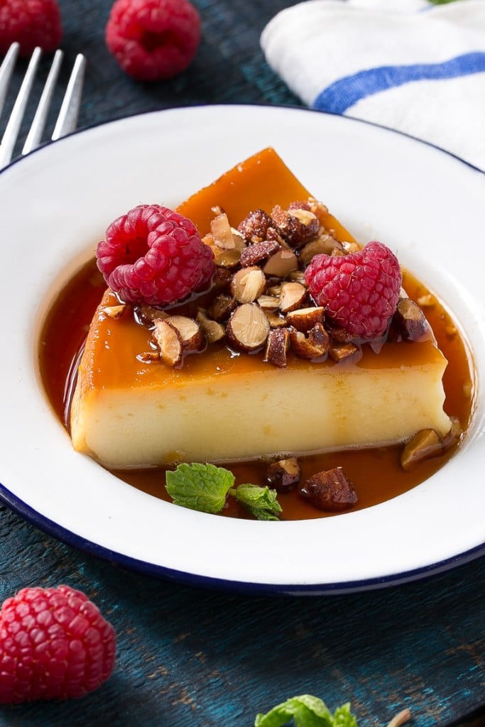 Este flan rico y cremoso está aromatizado con vainilla y almendras y se completa con almendras tostadas y frambuesas picadas.