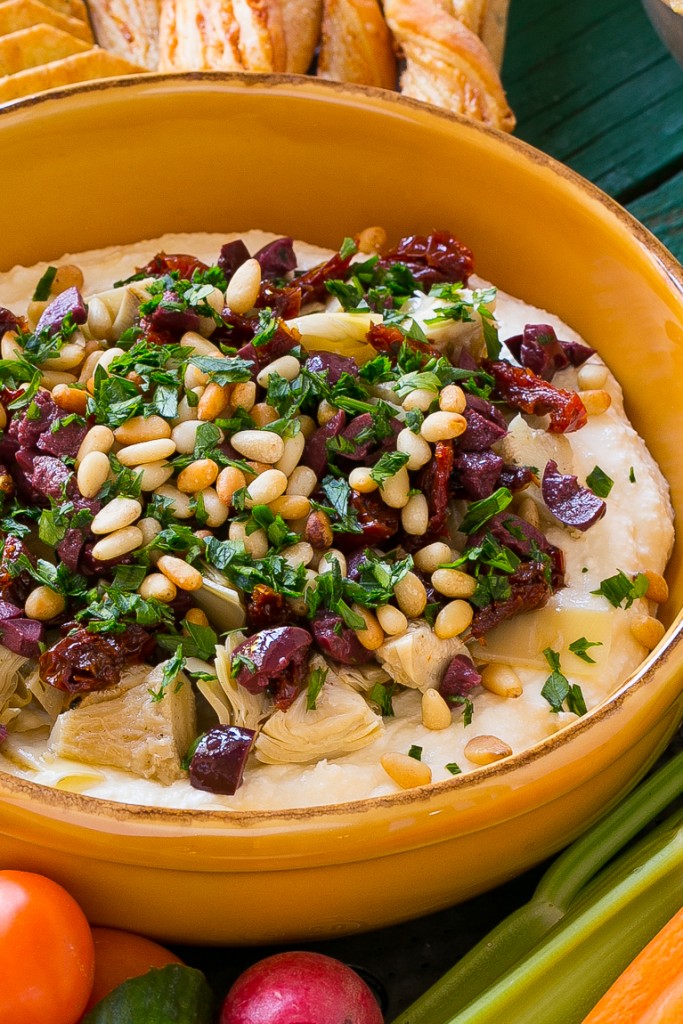 Esta salsa mediterránea en capas comienza con una base de queso feta batida y se cubre con alcachofas, aceitunas, tomates secos y piñones.  Listo en unos 10 minutos, ¡es el aperitivo perfecto para la fiesta!