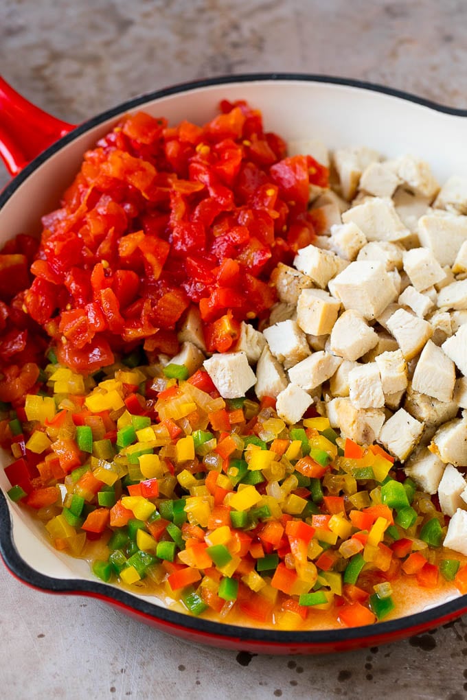 Dados de pollo, pimientos cocidos y tomates en una sartén.