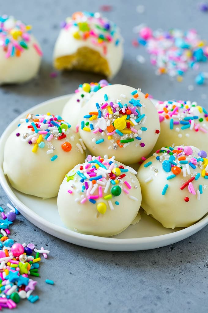 Receta de la bola de pastel | Pastel de trufa | Bocaditos de pastel # pastel # postre # postres #dinneratthezoo Un plato de bolas de bizcocho cubierto de chocolate blanco y chispitas de arco iris.
