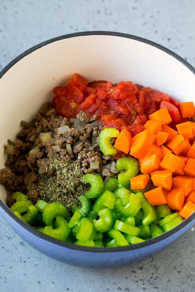 Carne molida, cebollas, tomates, zanahorias, apio, hierbas y especias en una olla.