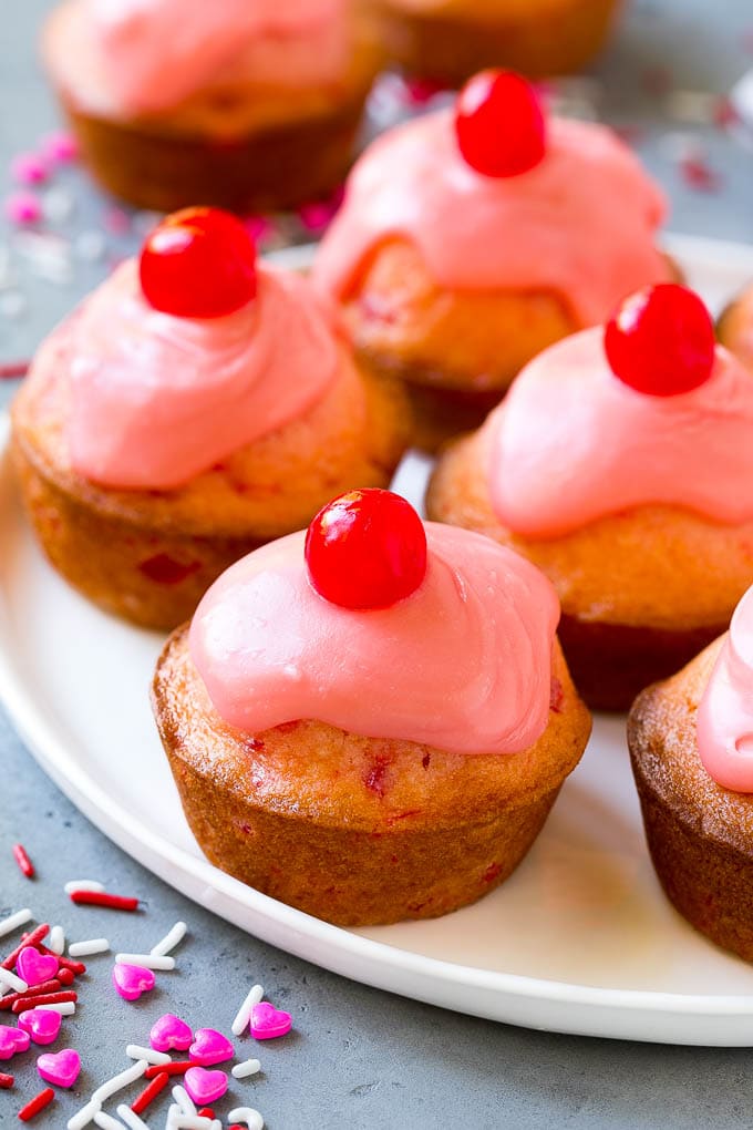 Muffins de cereza en un plato, cubiertos con glaseado y una cereza entera.