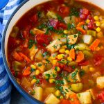 Una olla de sopa de pollo mexicana con vegetales coloridos y papas, cubierta con cilantro.