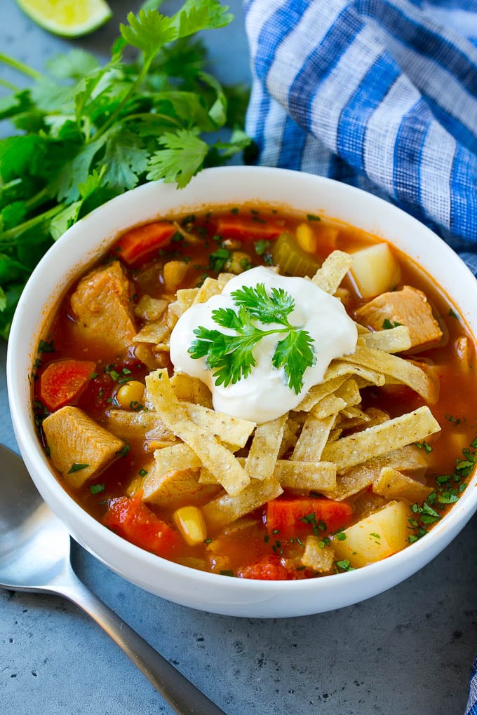 Un tazón de sopa de pollo mexicana cubierto con tiras de tortilla y crema agria.