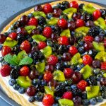 Pizza de frutas con corteza de galleta de azúcar y glaseado de queso crema, cubierta con bayas, kiwi y uvas.