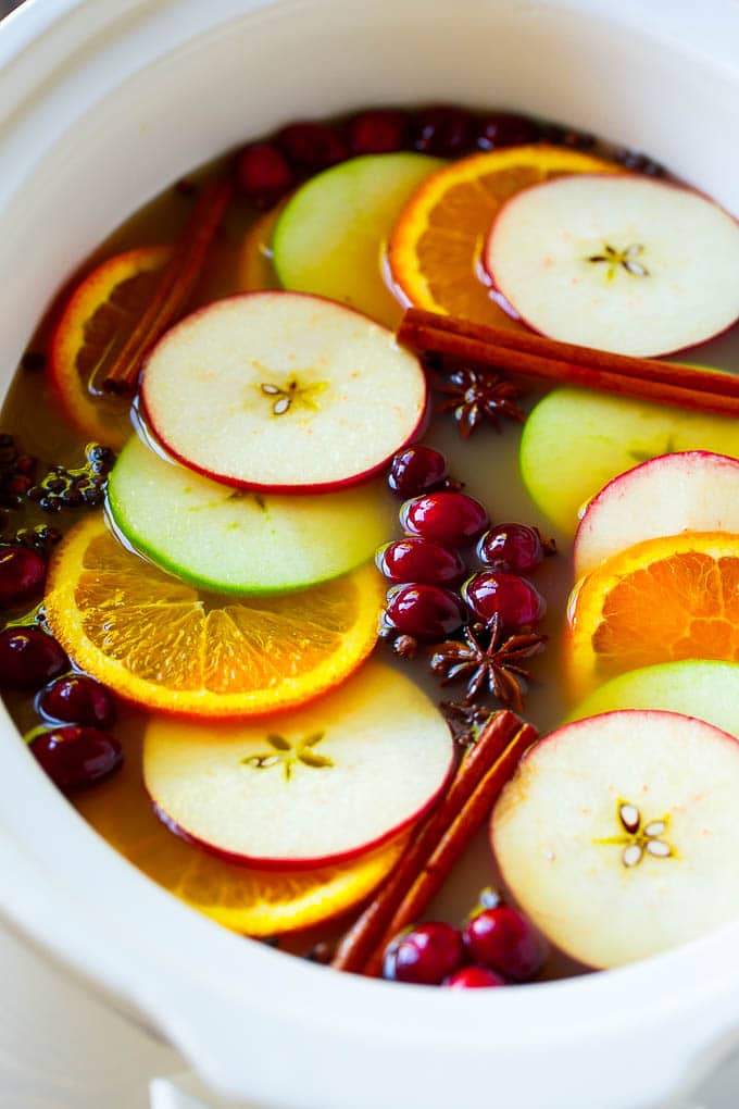Sidra de manzana en olla de cocción lenta con naranjas, rodajas de manzana, ramas de canela y arándanos.