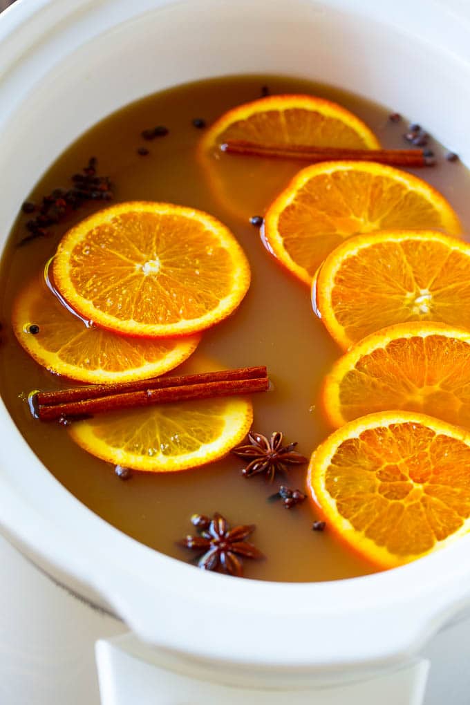 Sidra de manzana Crock Pot con rodajas de naranja y especias aromáticas.