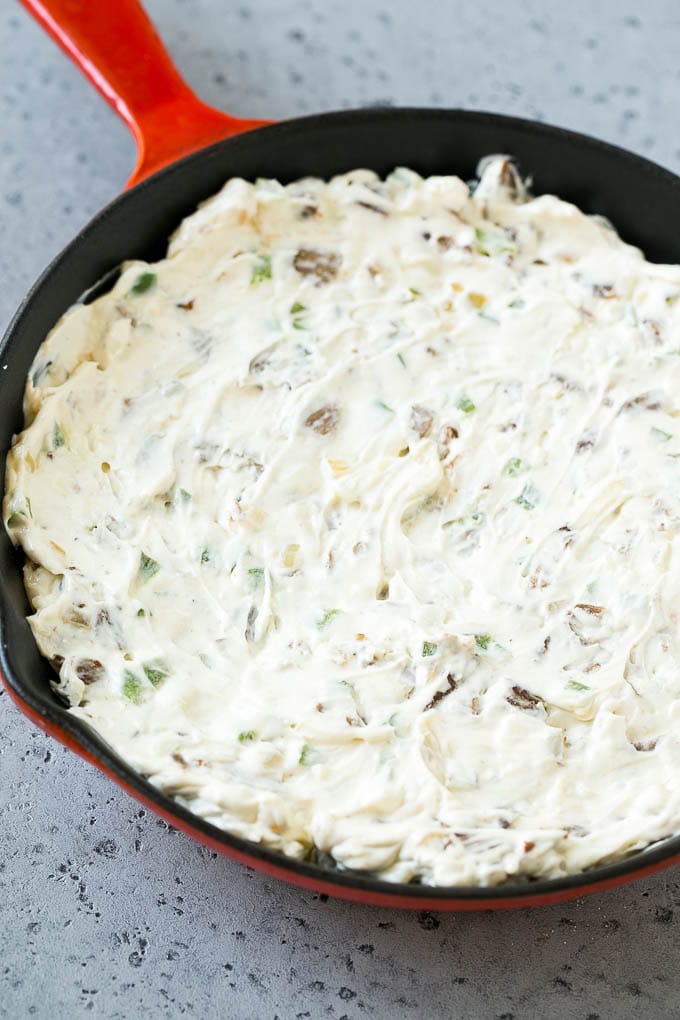 Bistec, pimientos y cebollas en una sartén, mezclado con queso crema.