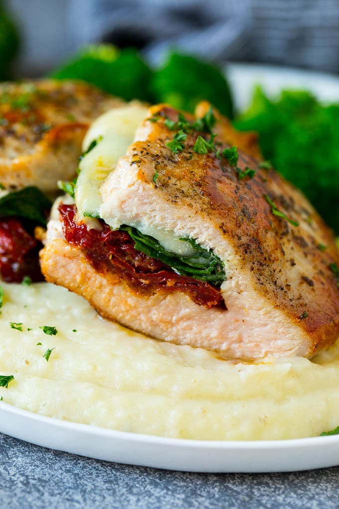 Una sección transversal de una chuleta de cerdo rellena servida con puré de papas y brócoli.