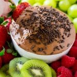 Una fresa en un cuenco de salsa de frutas de chocolate rodeada de un surtido de frutas.