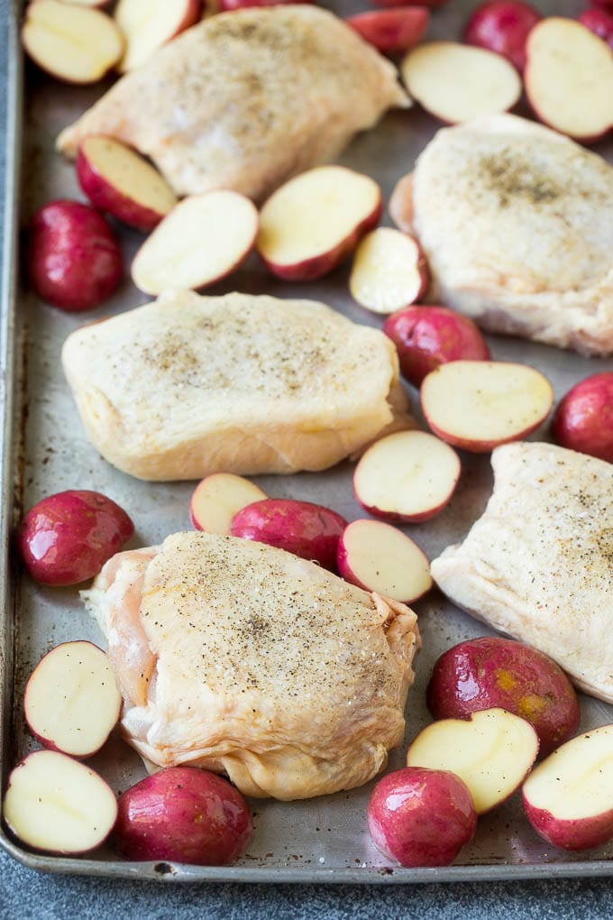 Receta de pollo balsámico | Pollo en un plato | Pollo glaseado # pollo # espárragos # papas # cena # sin gluten #dinneratthezoo Muslos de pollo y papas cortadas por la mitad en una bandeja para hornear.