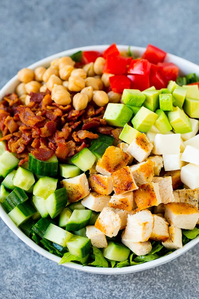 Un tazón de lechuga cubierto con pollo molido, pepino, aguacate, tocino, garbanzos y tomates.