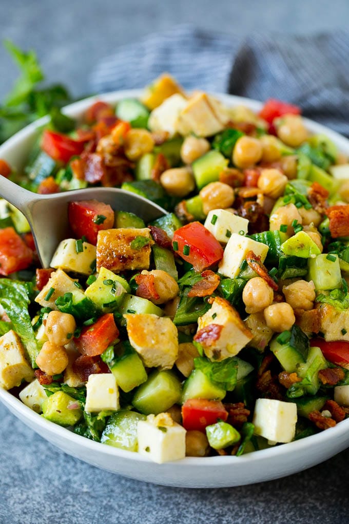 Una cuchara para servir en un cuenco de ensalada picada aderezada con cebollino fresco.