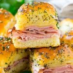 Una pila de deslizadores de jamón y queso cubiertos con mantequilla de amapola y perejil.