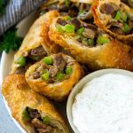 Un plato de rollos de huevo Philly Cheesesteak rellenos con bistec cortado en cubitos, pimientos, cebollas y queso.