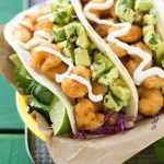 Esta receta de taco de camarones fritos es un manojo de camarones crujientes cubiertos con ensalada de col con cilantro y salsa de aguacate, luego se rellena en tortillas de harina tibias.  ¡Es una comida rápida y fácil que sabe a comida de un restaurante!  Anuncio de #ShrimpItUp