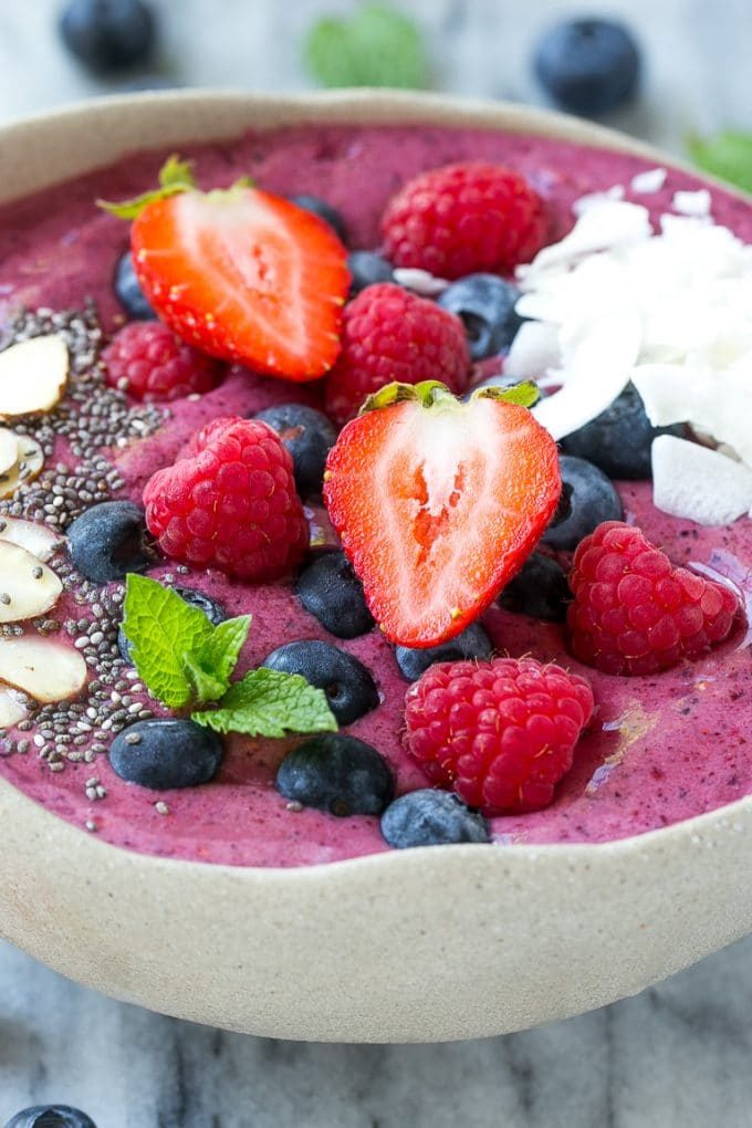 Un tazón de acai hecho con bayas congeladas, luego adornado con frutas frescas, coco y semillas.