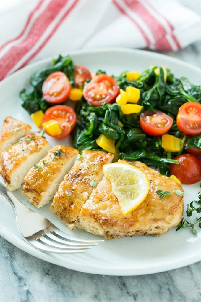 Un plato de pechuga de pollo a la plancha, servido con espinacas y verduras.