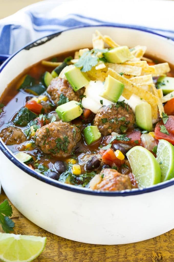 Una olla de sopa de albóndigas con maíz, frijoles y zanahorias, cubierta con crema agria y aguacate.