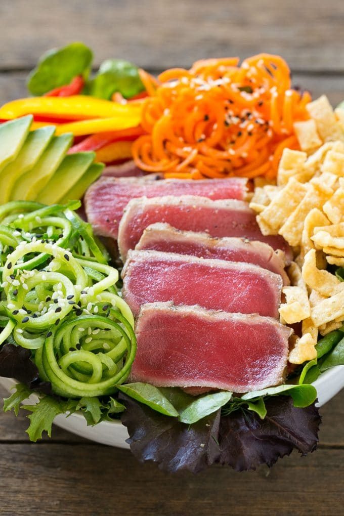 Un tazón de ensalada de atún ahi con atún braseado en rodajas finas y una variedad de verduras de colores.