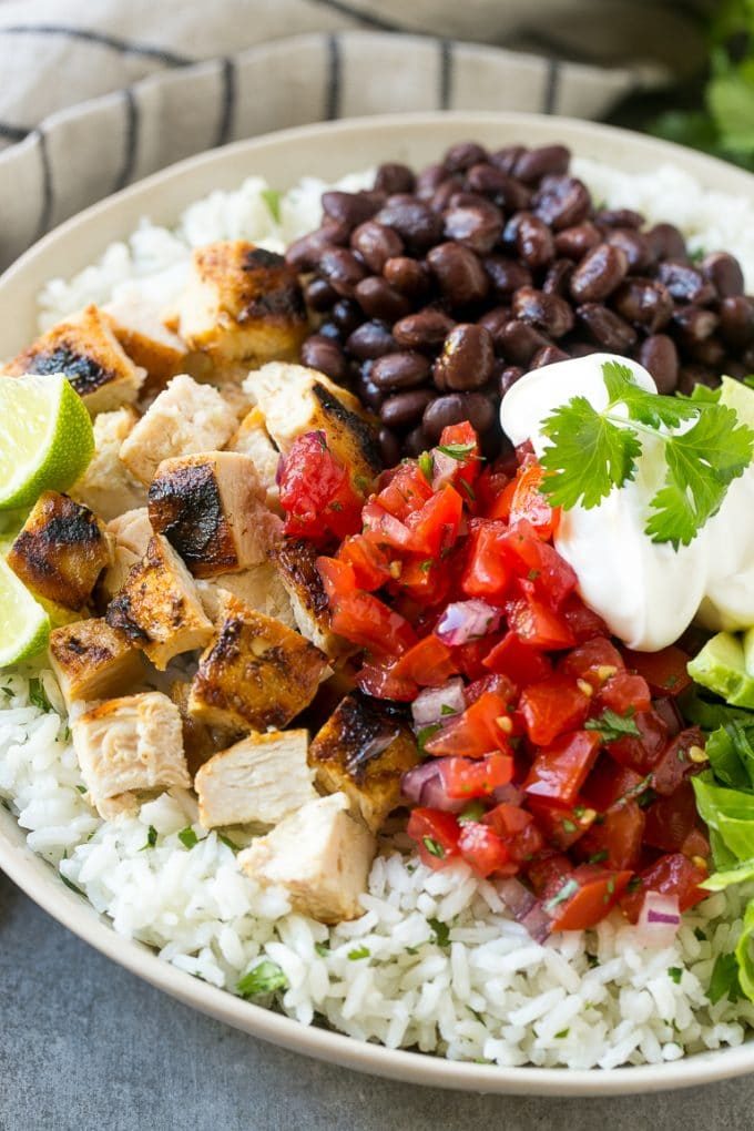 Un tazón de burrito de pollo a la parrilla con salsa, aguacate, crema agria, frijoles negros y arroz.