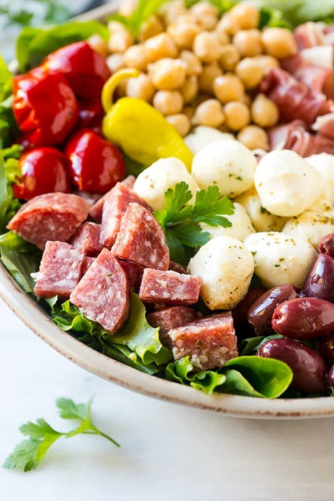 Un lecho de verduras coronado con una ensalada de aperitivo a base de embutidos, quesos, frijoles y verduras.