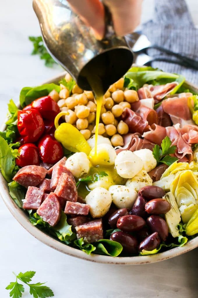 Se vierte una jarra de aderezo sobre una ensalada de aperitivo.