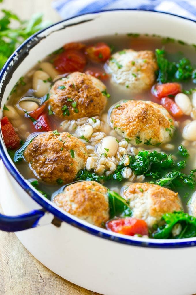 Una olla de sopa de farro con albóndigas, frijoles blancos y repollo negro.