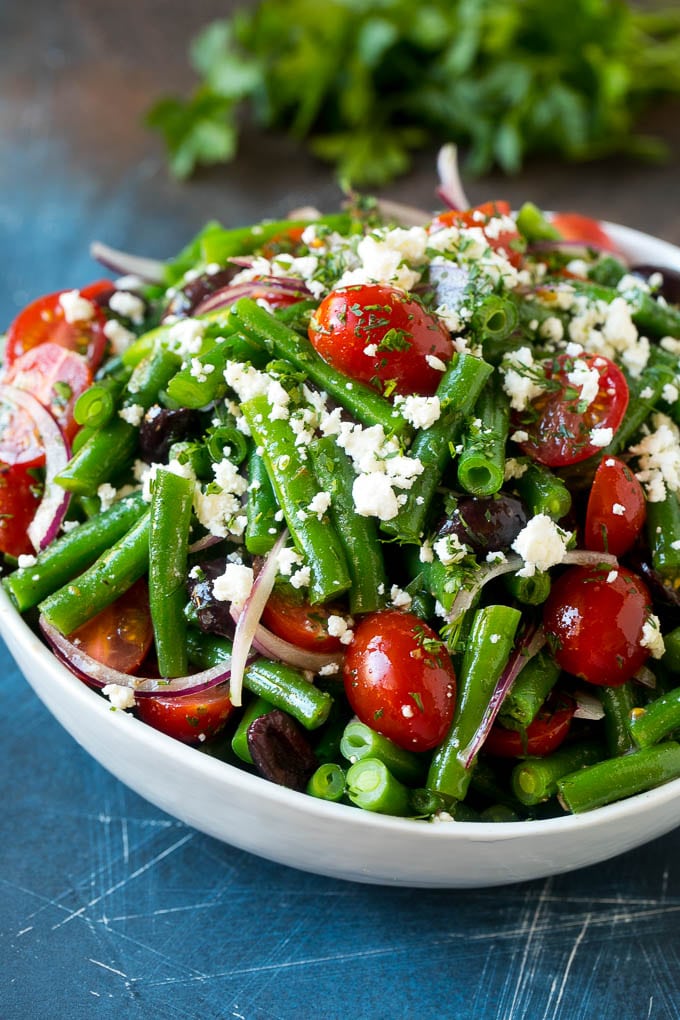 Ensalada de judías verdes mezclada con un aderezo y cubierta con queso feta y hierbas.