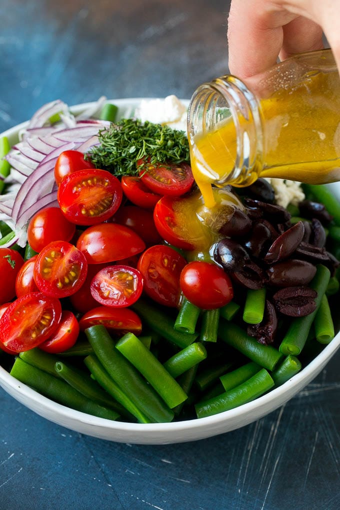 El aderezo se vierte sobre judías verdes, tomates cherry, aceitunas, hierbas y cebollas.