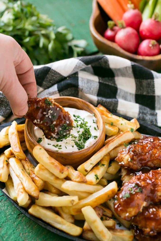 Una mano mojando un dedo de pollo en la salsa.