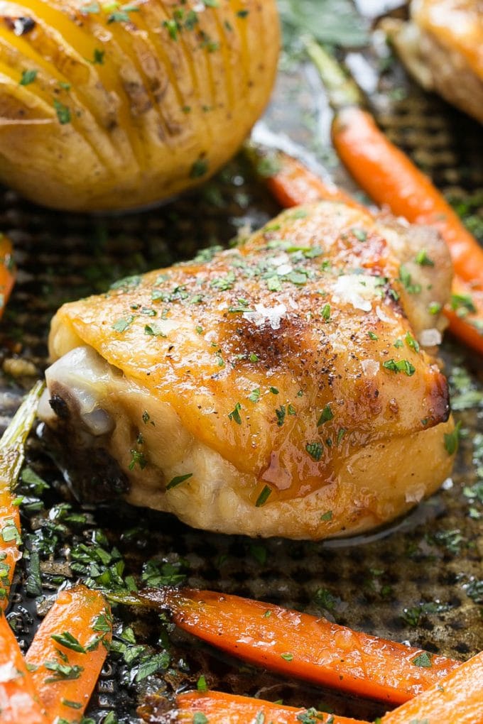 Una pierna de pollo asada rodeada de zanahorias y patatas.